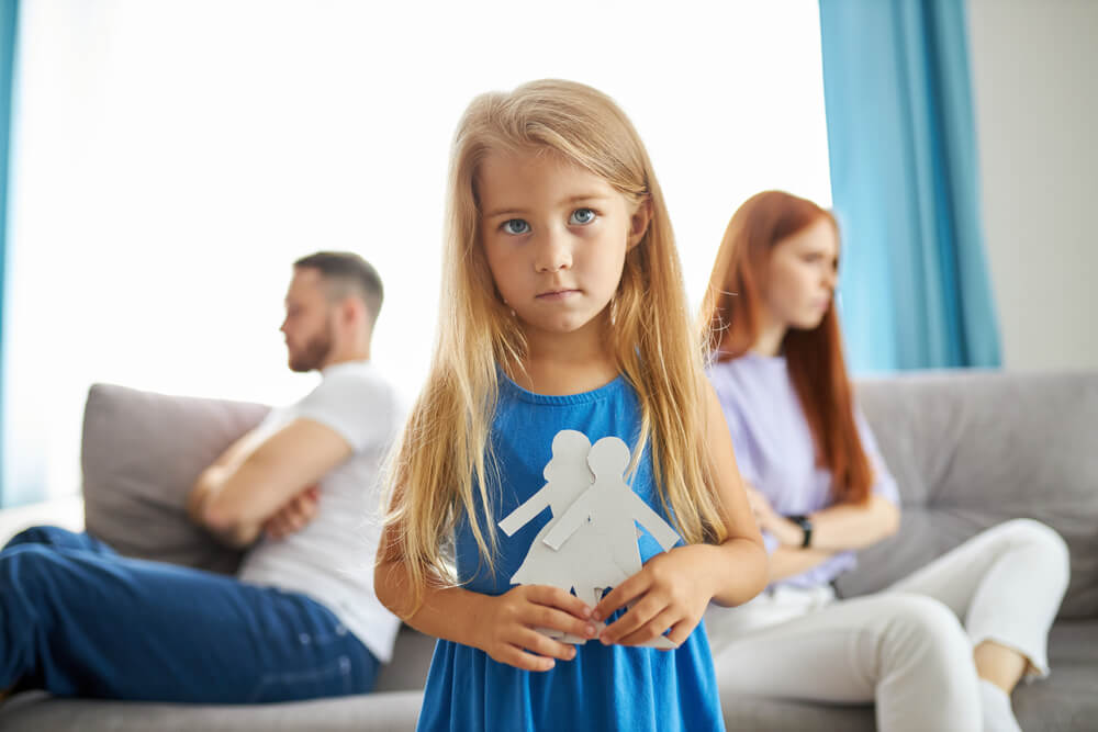 Sad girl holding paper dolls representing her parents.