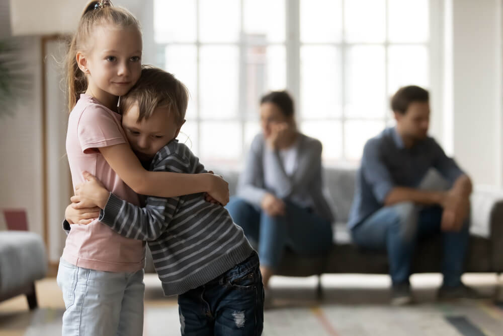 Siblings hugging each other while parents are arguing.