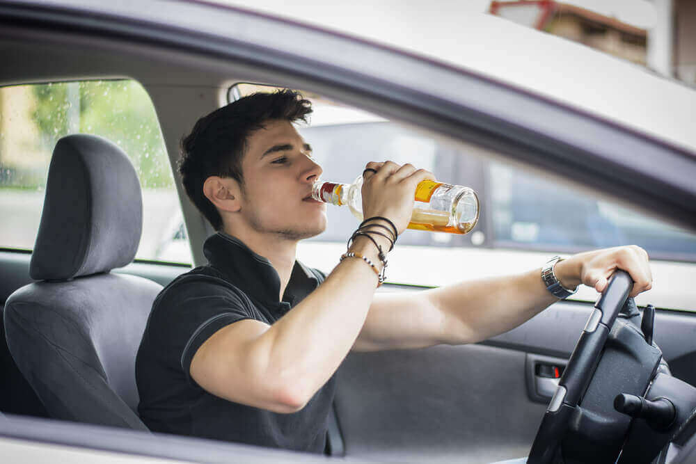 Young driver drinking beer while driving.